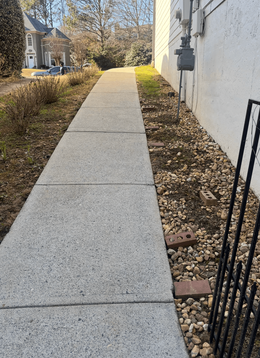 Concrete sidewalk stretching alongside a white house with a rock border and red bricks.